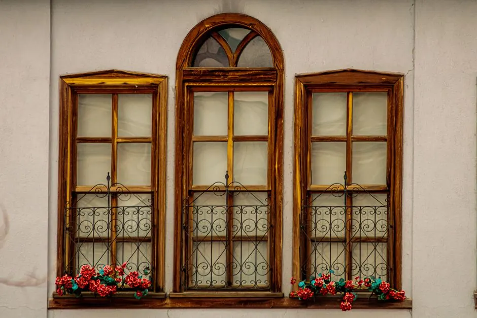 Three wooden windows with vibrant flower boxes on a vintage facade.
